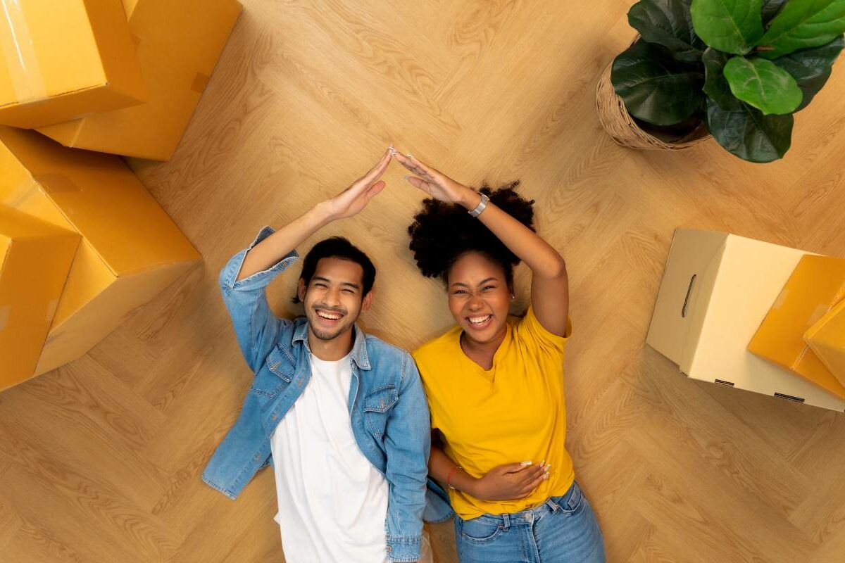 Young couple man and woman looking satisfied sitting on the floor hugging during moving to new apartment unpacking boxes.