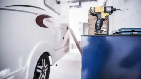 A shot of an RV parked in a garage next to a workbench with a power drill in the shot.