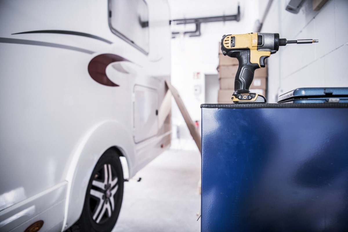 A shot of an RV parked in a garage next to a workbench with a power drill in the shot.