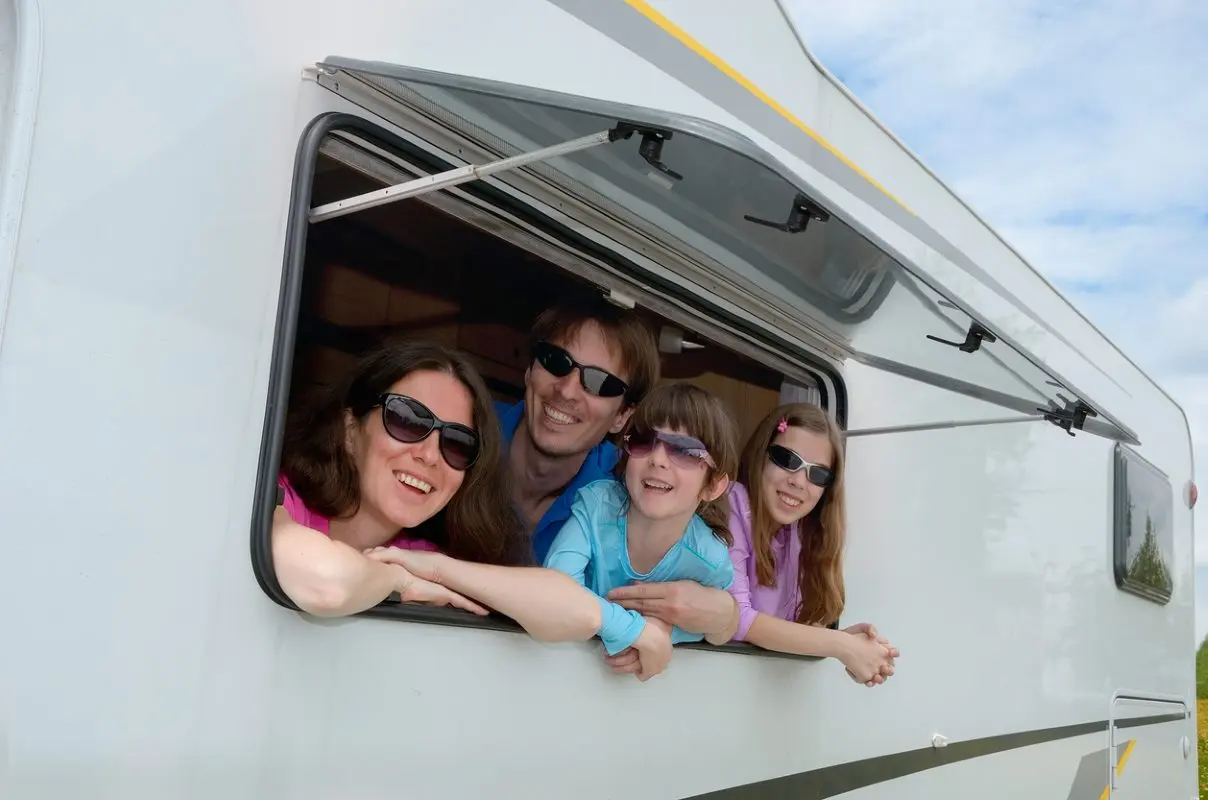 Family smiling and leaning out of the window of an RV with sunglasses on.