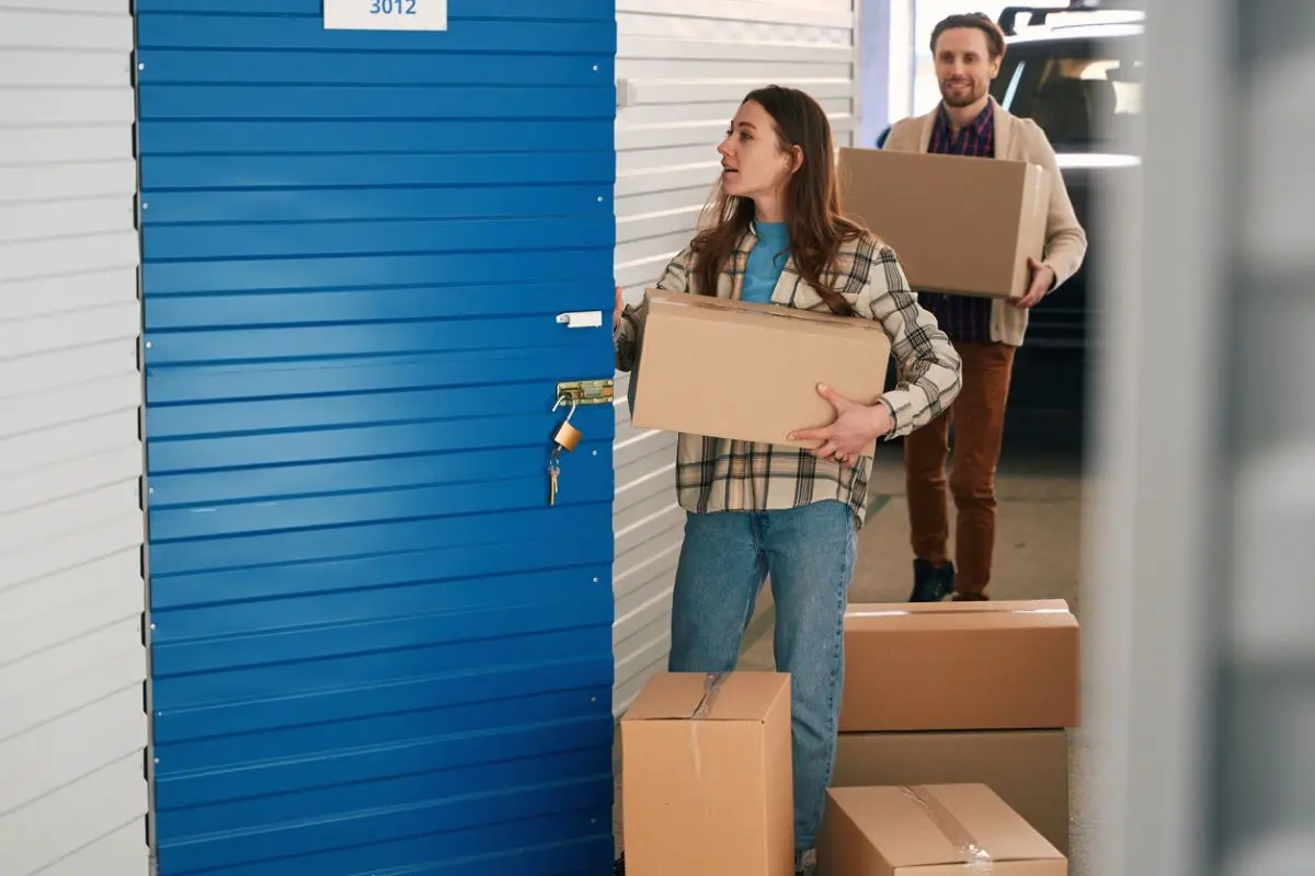 Young woman and man putting big cardboard boxes into their storage unit.