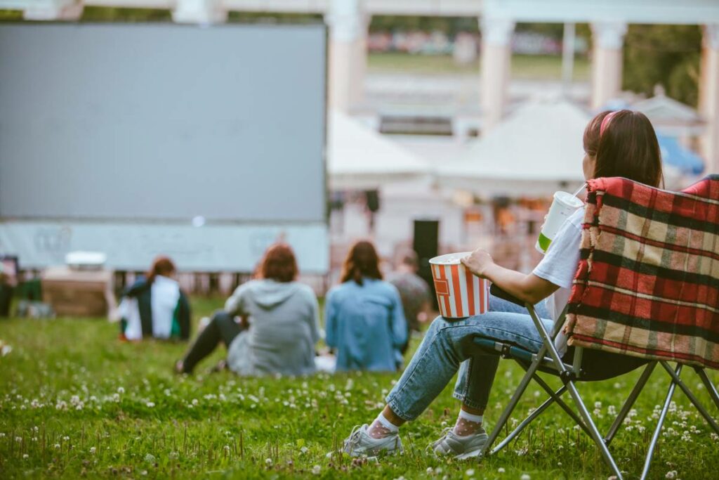 Woman sitting in camping chair watching movie at open air cinema
