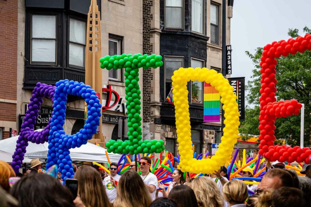 People marching in a PRIDE parade with colorful balloons that spell "Pride"