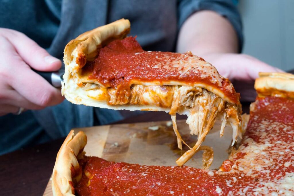 Top view of Chicago pizza. Woman hands cutting Chicago style deep dish Italian cheese pizza with tomato sauce and beef meet