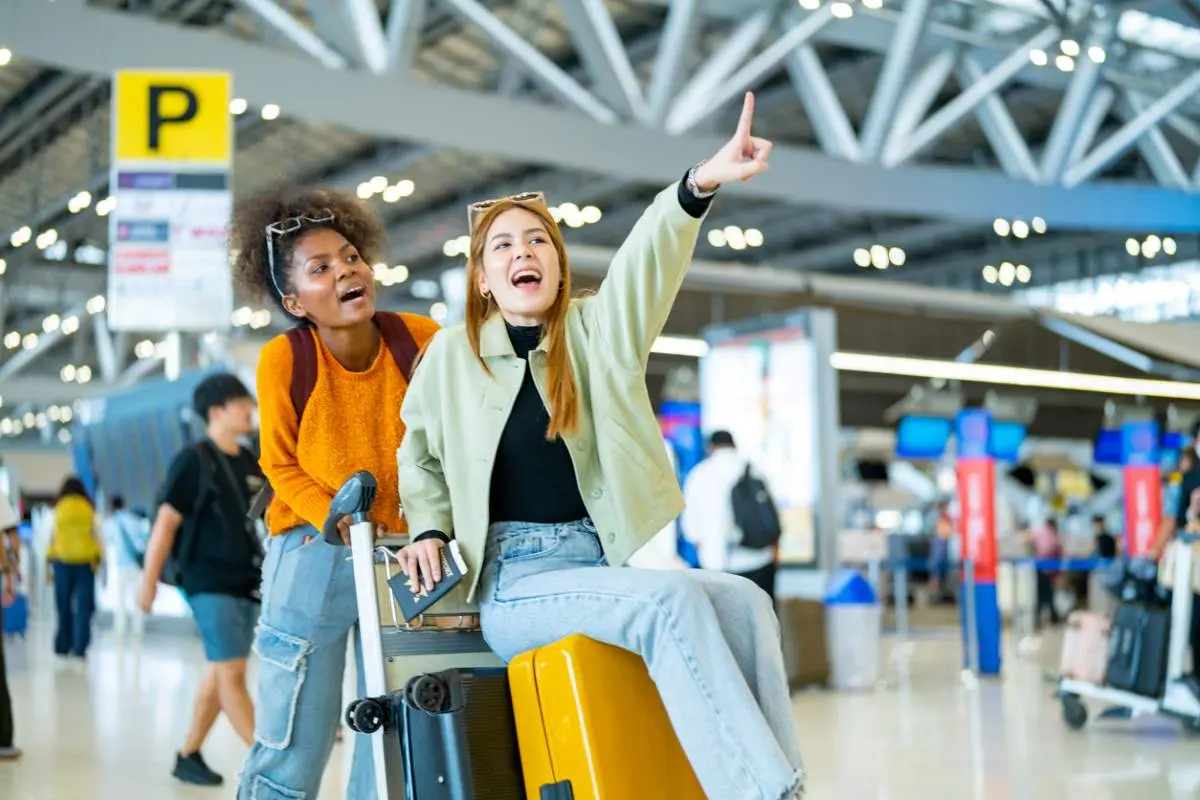 Two woman friends with luggage walking together at Airport terminal. 