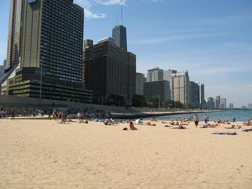 People laying out in the sand on Ohio State Beach with city buildings in the background. 