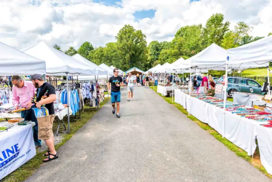 A sidewalk lined with booths selling goods and people shopping in the sun.