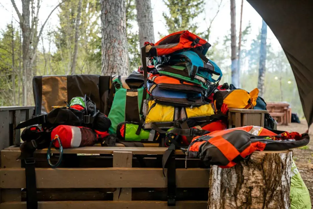 A pile of colorful backpacks and camping gear stacked on a picnic table.