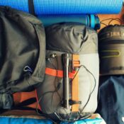 A flat-lay composition of camping equipment with a sleeping bag, backpack, boots, and more.
