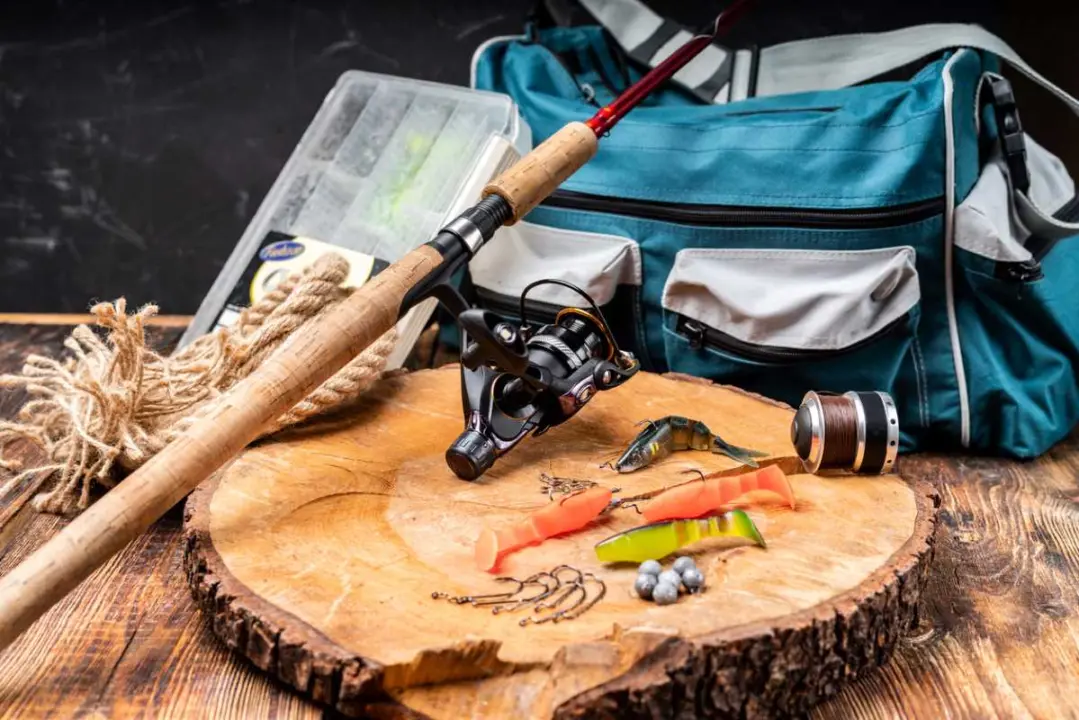 Fishing items, including a rod, tackle, and bag, on a wooden stump.