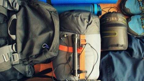 A flat-lay composition of camping equipment with a sleeping bag, backpack, boots, and more.