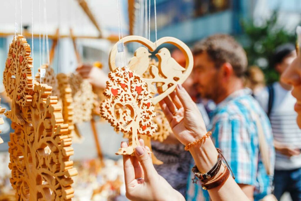 A tourist at a festival chooses between handmade, wood-carved gifts.