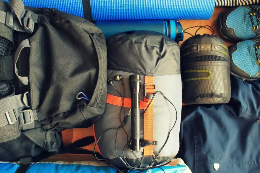 A flat-lay composition of camping equipment with a sleeping bag, backpack, boots, and more.