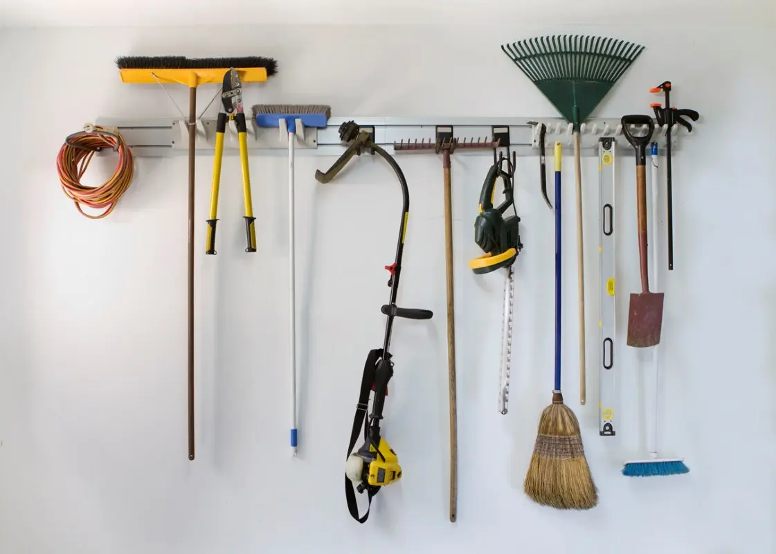 Common gardening tools, including a rake, shovel, chainsaw, and weed whacker, hang on a rack.