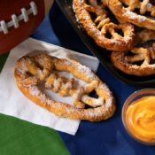 A football-shaped pretzel with cheese on a table at a tailgate.