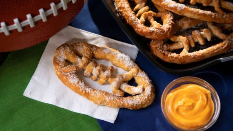 A football-shaped pretzel with cheese on a table at a tailgate.