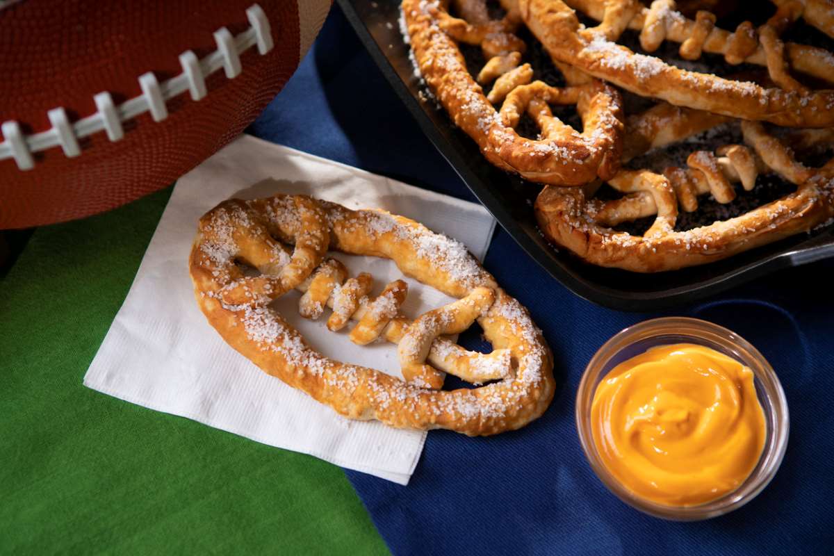 A football-shaped pretzel with cheese on a table at a tailgate.