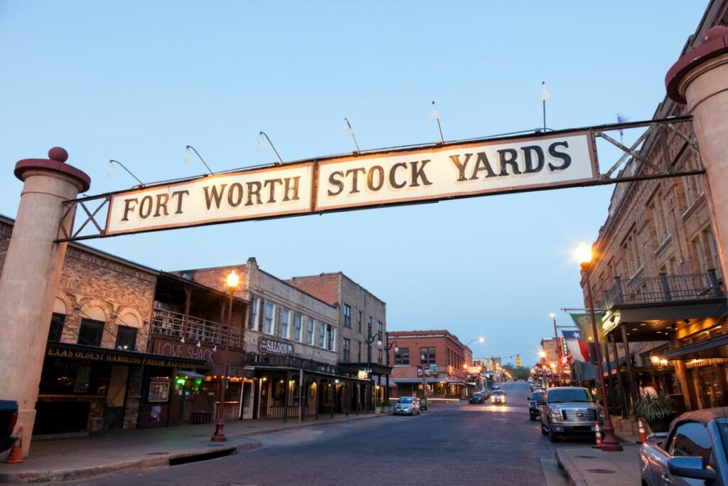 Fort Worth Stock Yards gates with cars on the streets and evening hue. 