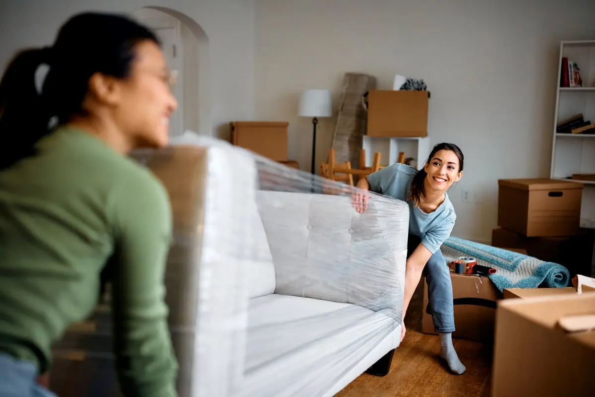 Happy women carrying sofa into their new apartment