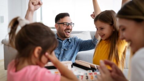 : A young family plays a board game surrounding a table