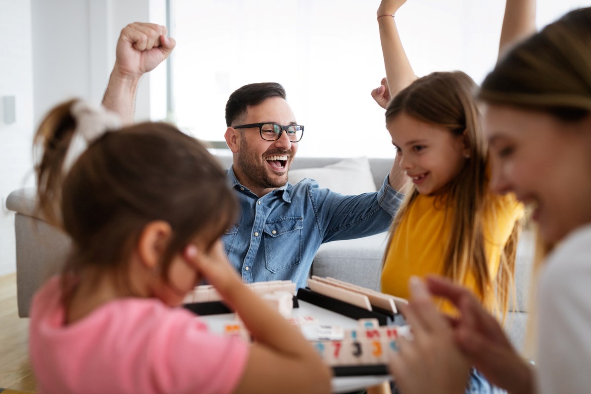 : A young family plays a board game surrounding a table