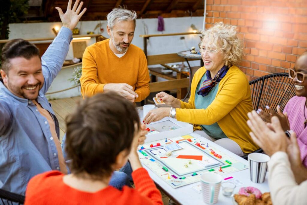 A group of family and friends surround a table, playing Sorry! and celebrating a win. 