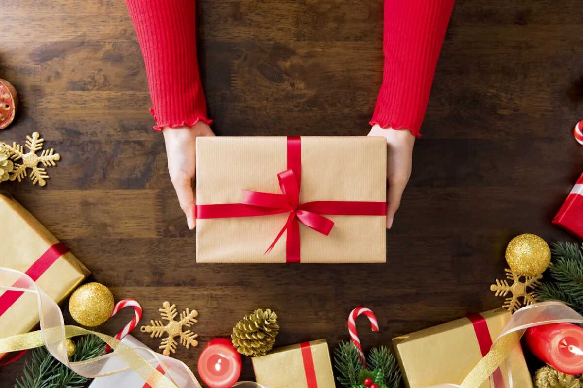 A woman’s hands holding a delicately wrapped Christmas gift on a festive table.