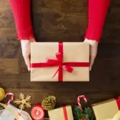 A woman’s hands holding a delicately wrapped Christmas gift on a festive table.