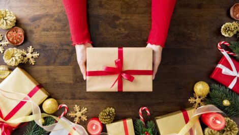 A woman’s hands holding a delicately wrapped Christmas gift on a festive table.