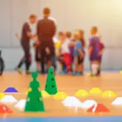 Soccer cones set up on the floor with a soccer team blurred in the background.