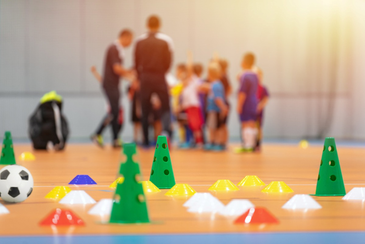 Soccer cones set up on the floor with a soccer team blurred in the background.