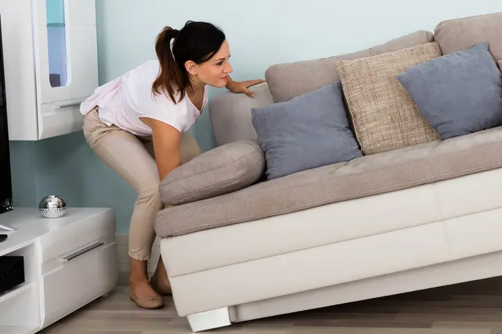 A woman helps move a couch to a different spot in the living room.