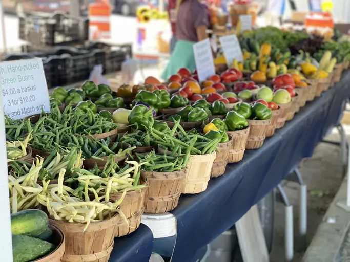 Wooden baskets filled with fresh fruits and vegetables line a farmers market vendor’s table. 